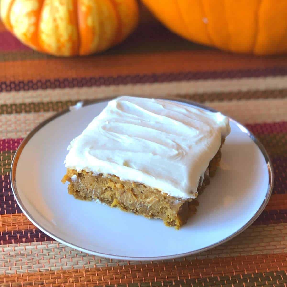 A gluten free pumpkin bar with white frosting on a dessert plate.