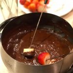 A banana and strawberry being dipped in dairy free chocolate fondue