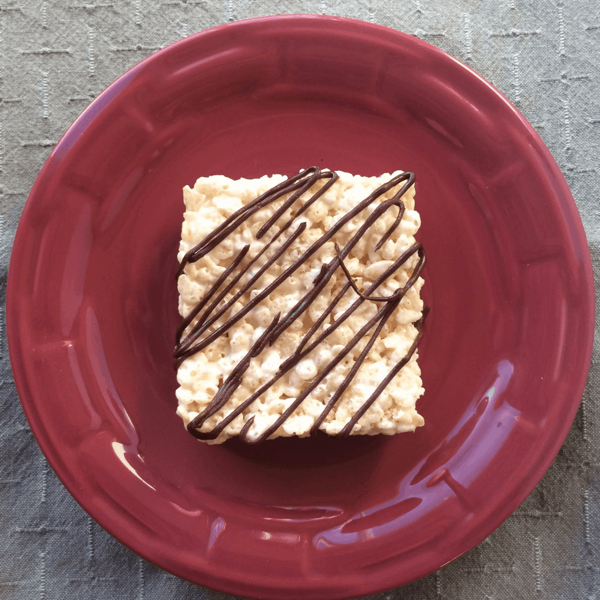 A gluten and dairy free rice krispie treat drizzled with chocolate on a plate.