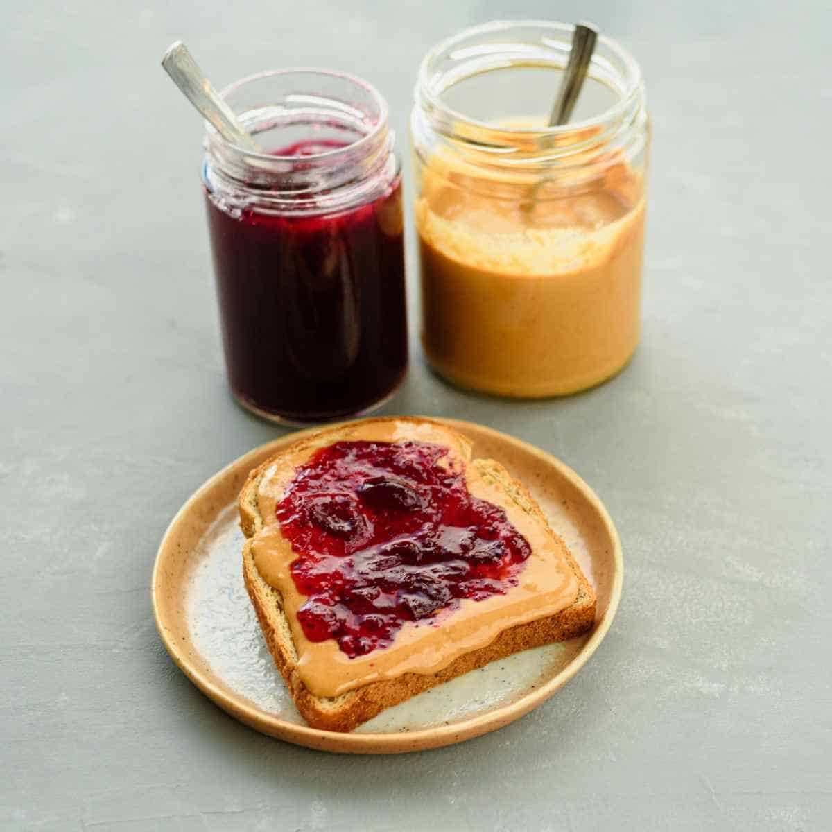 A jar of peanut butter and jelly with separate utensils to prevent cross-contact.