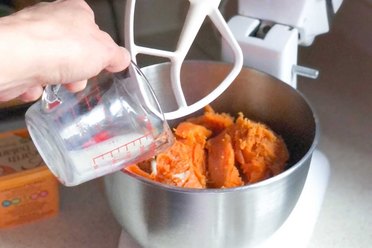 Dairy free milk being added to a mixing bowl with sweet potatoes