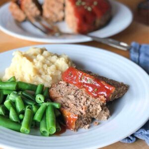 Eggless meatloaf on a plate with green beans and mashed potatoes