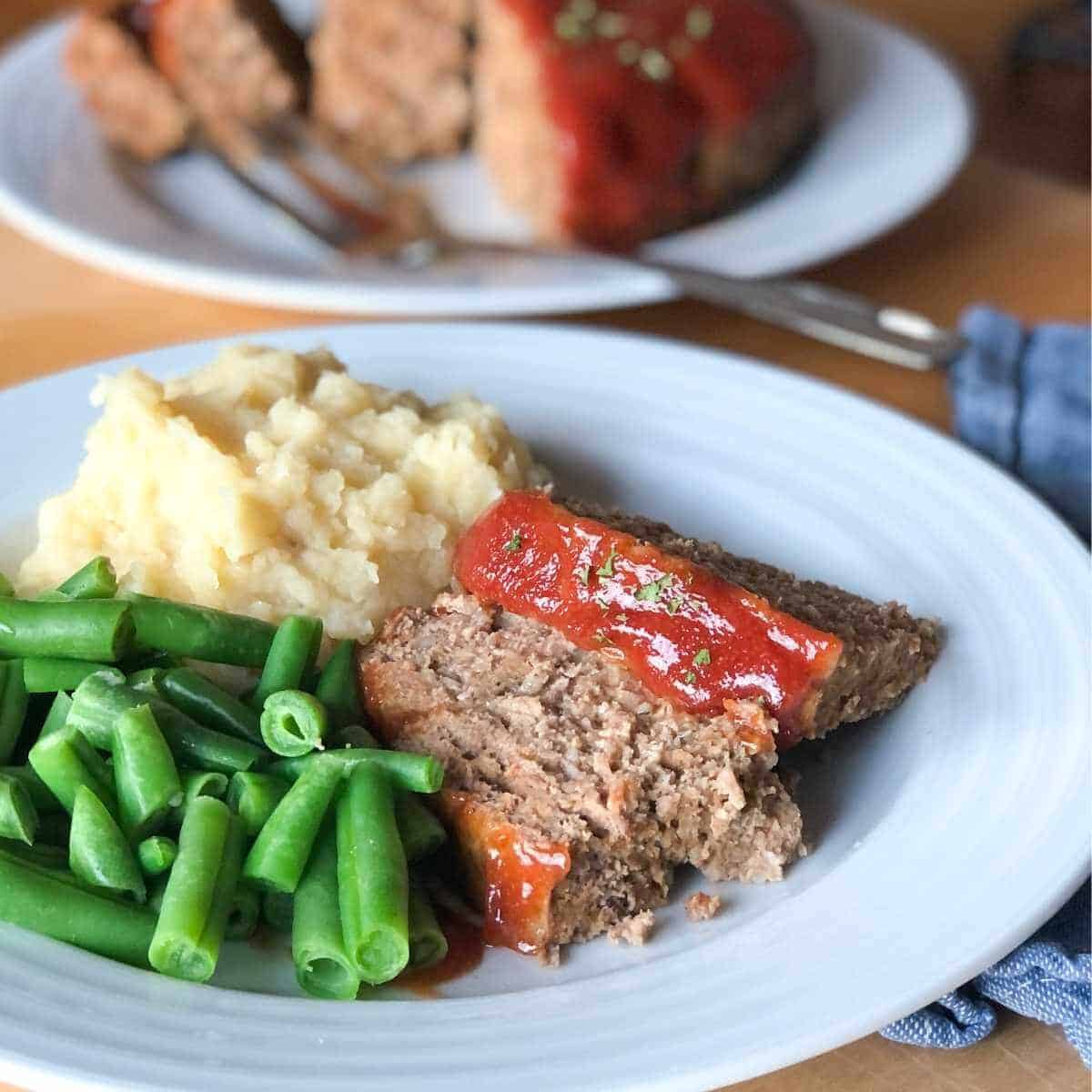 Eggless meatloaf on a plate with mashed potatoes and green beans