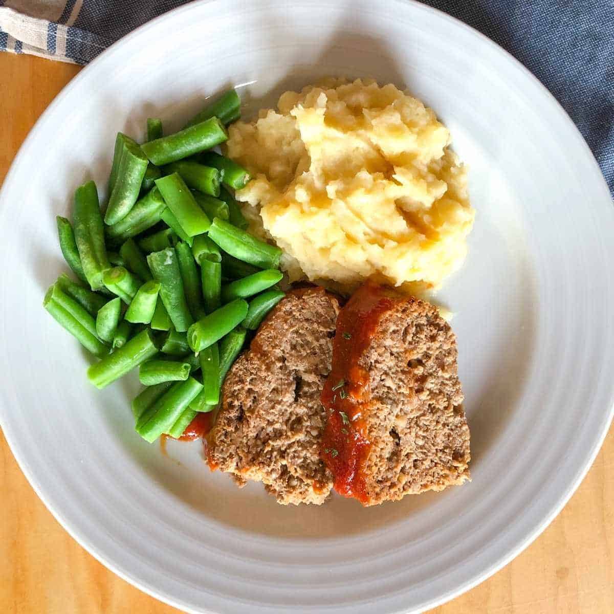 An overhead view of a plate with eggless meatloaf, mashed potatoes, and green beans.