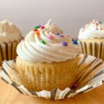 A gluten free dairy free cupcake topped with vanilla frosting and multi-color sprinkles