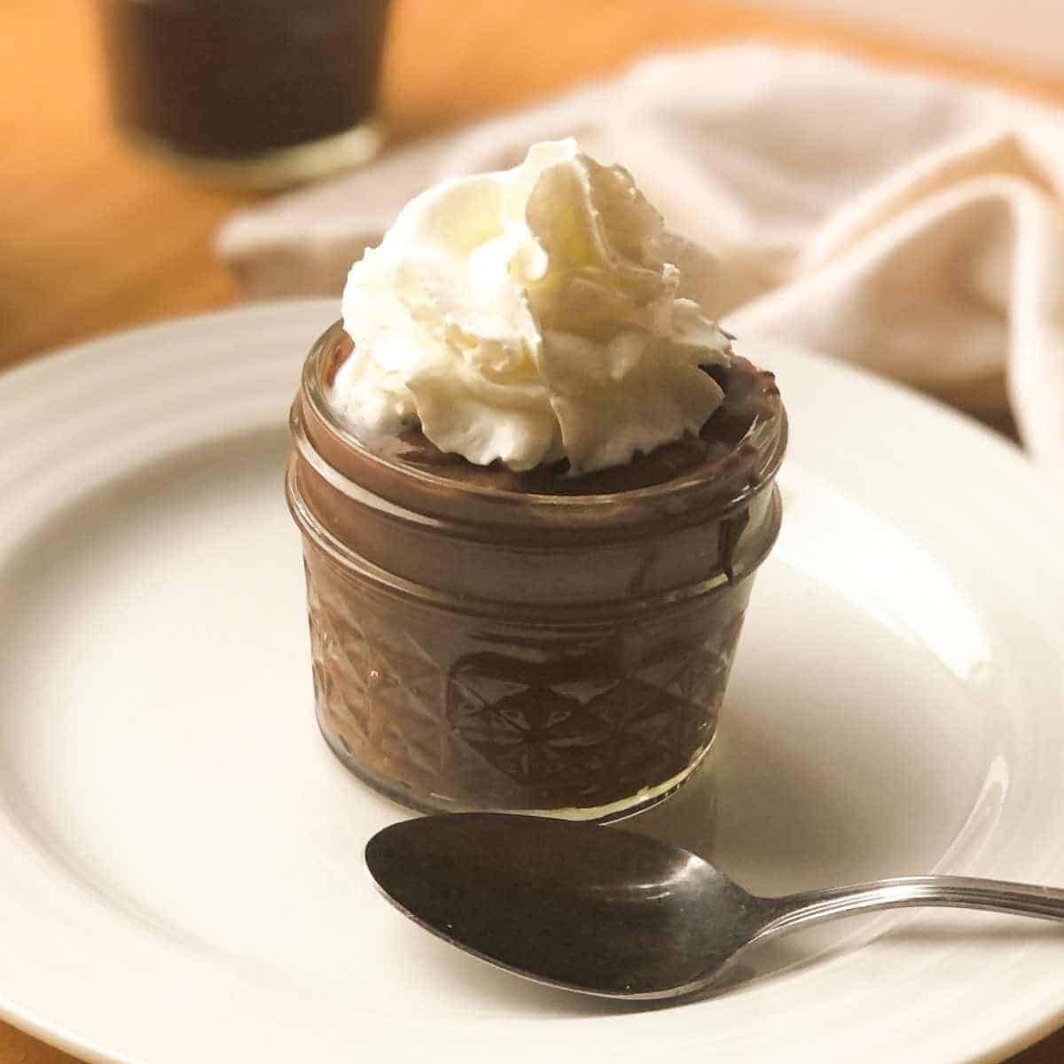 A small jar with oat milk chocolate pudding topped with dairy free whipped cream