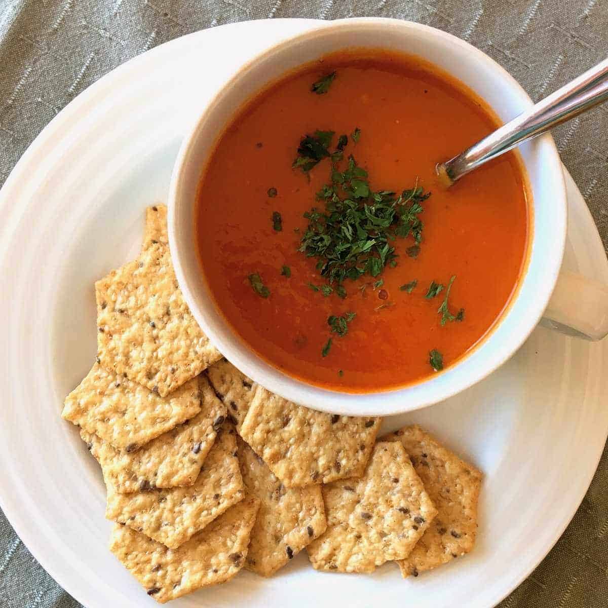 A cup of gluten free tomato soup with crackers on the side