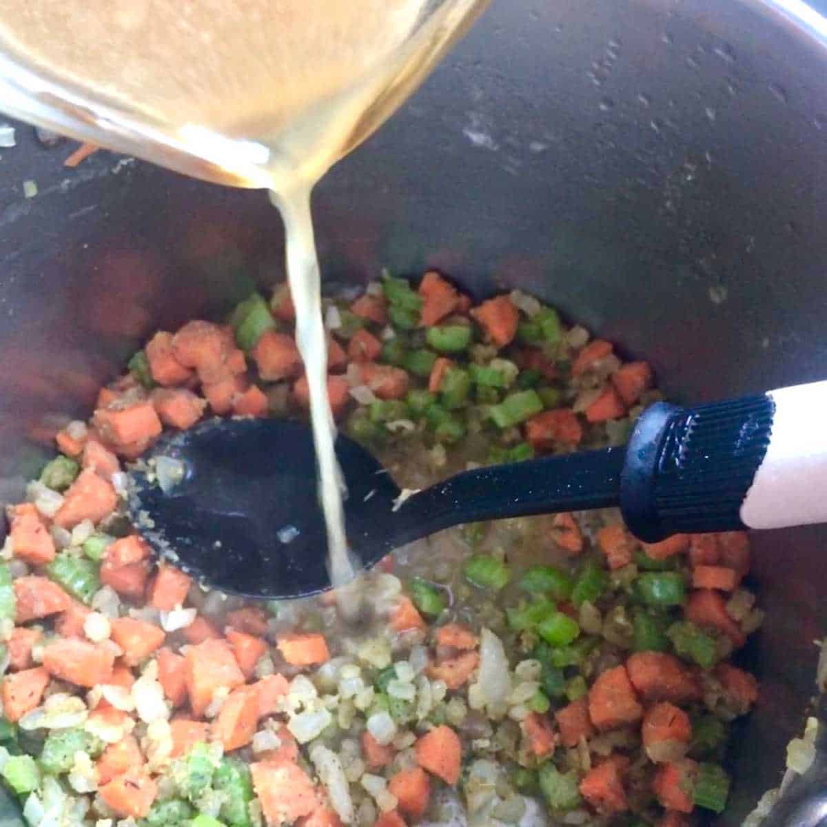 Chicken broth and dairy free milk being poured over vegetables coated in gluten free flour