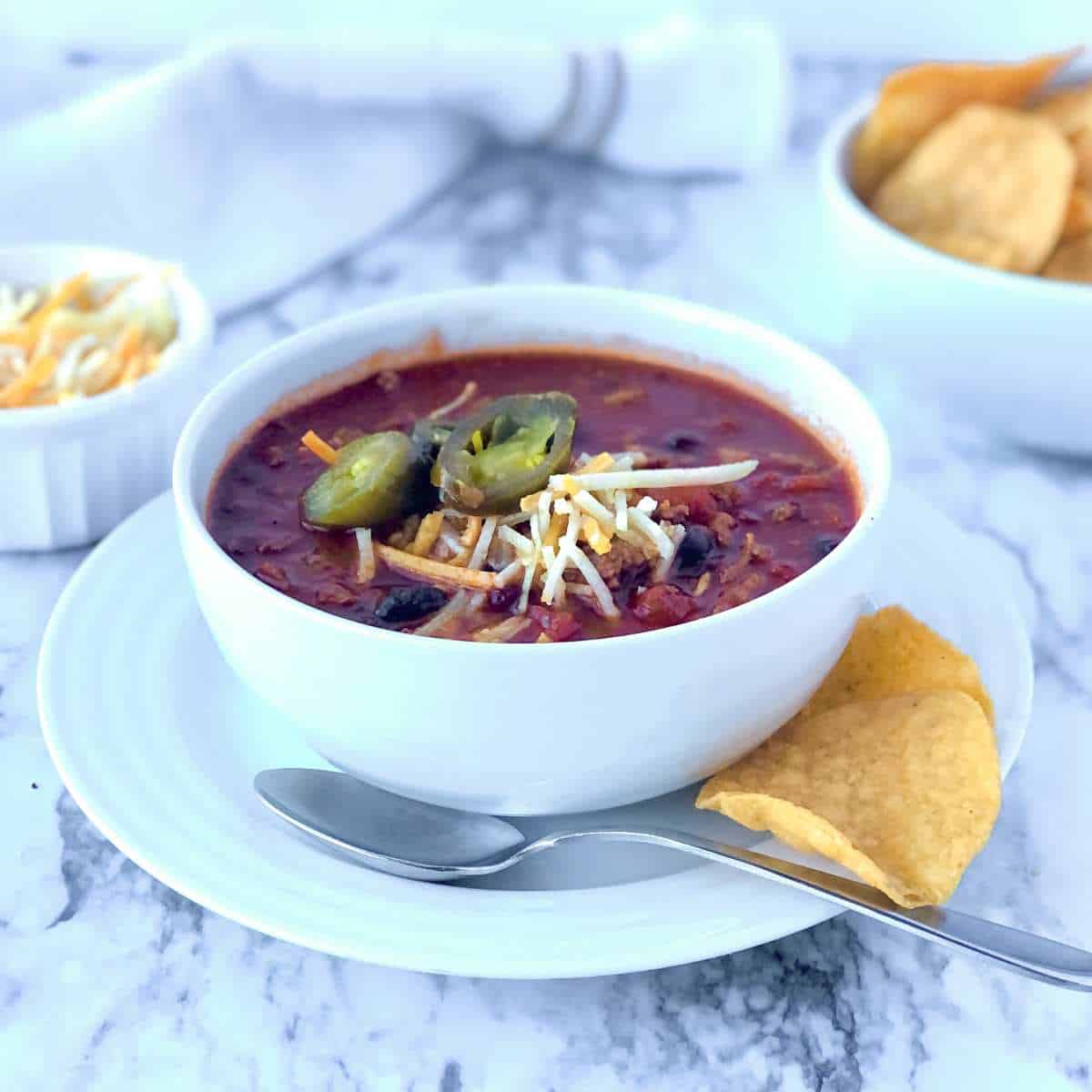 A bowl of gluten free chili topped with dairy free cheese and jalapenos