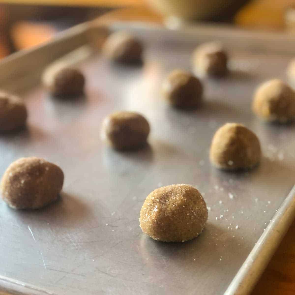 Gluten free ginger cookie dough balls coated in sugar on a baking sheet.