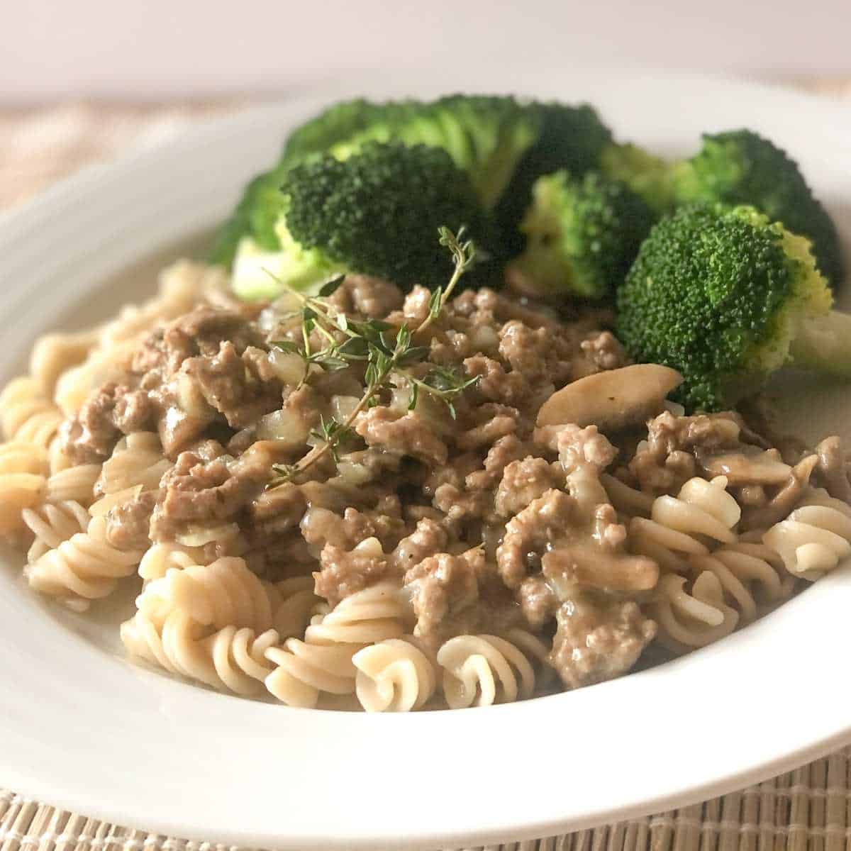 Gluten and dairy free turkey stroganoff served over gluten free noodles with a side of steamed broccoli on a plate.