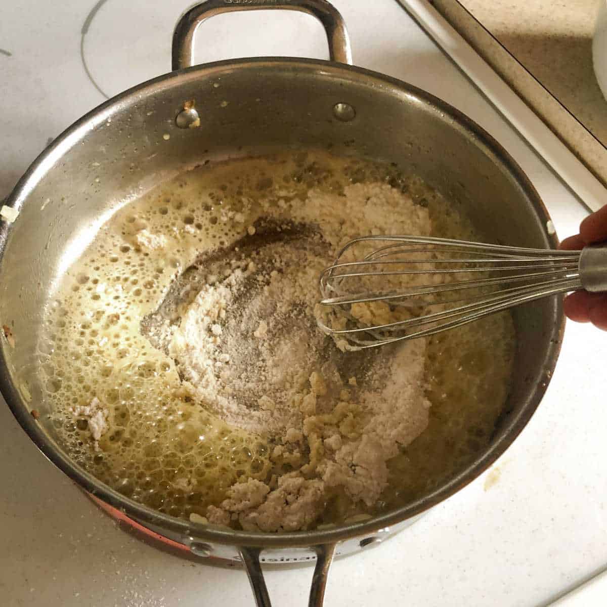 Gluten free flour being whisked into melted dairy free butter in a skillet.