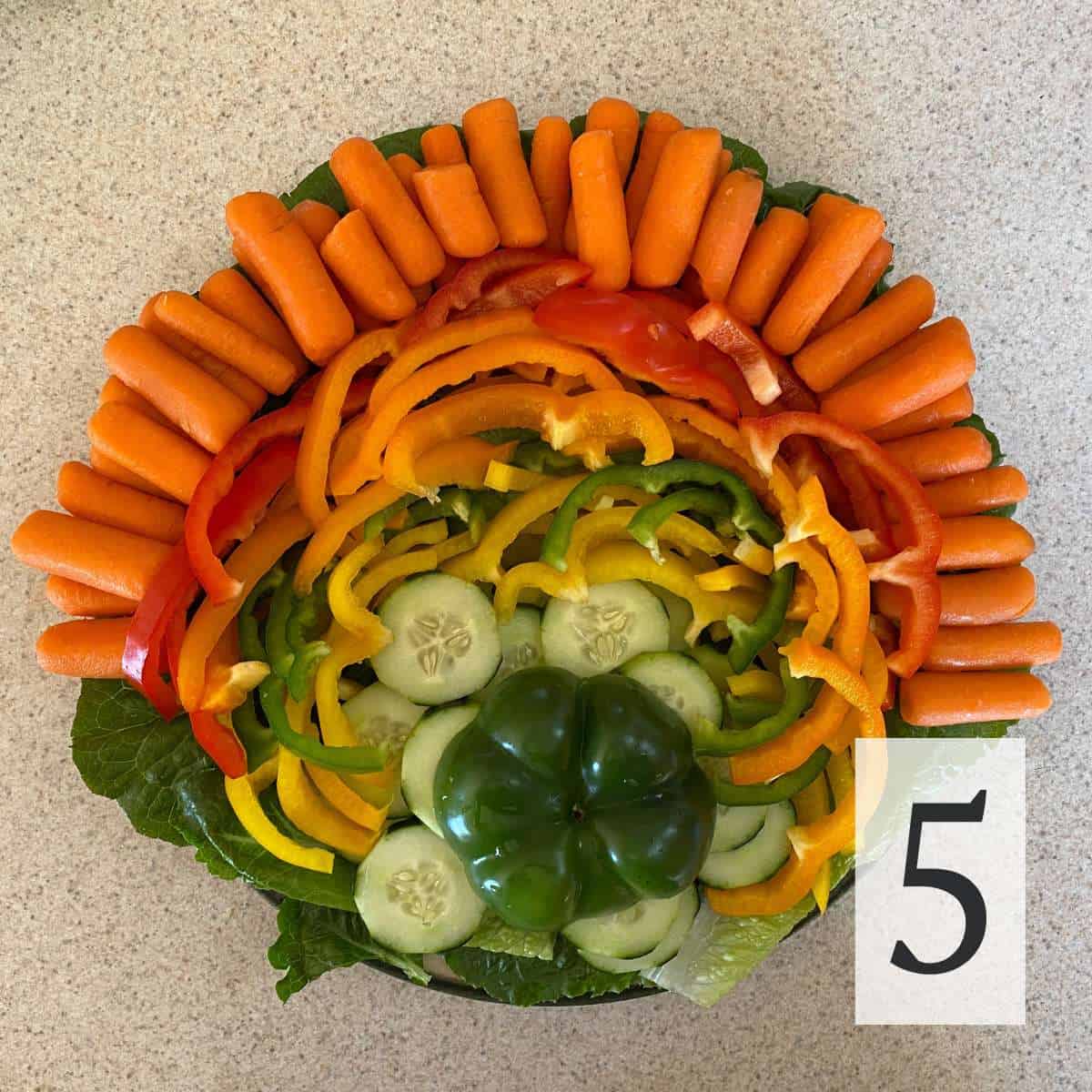 Cucumbers. bell peppers, and baby carrots arranged on a round platter.