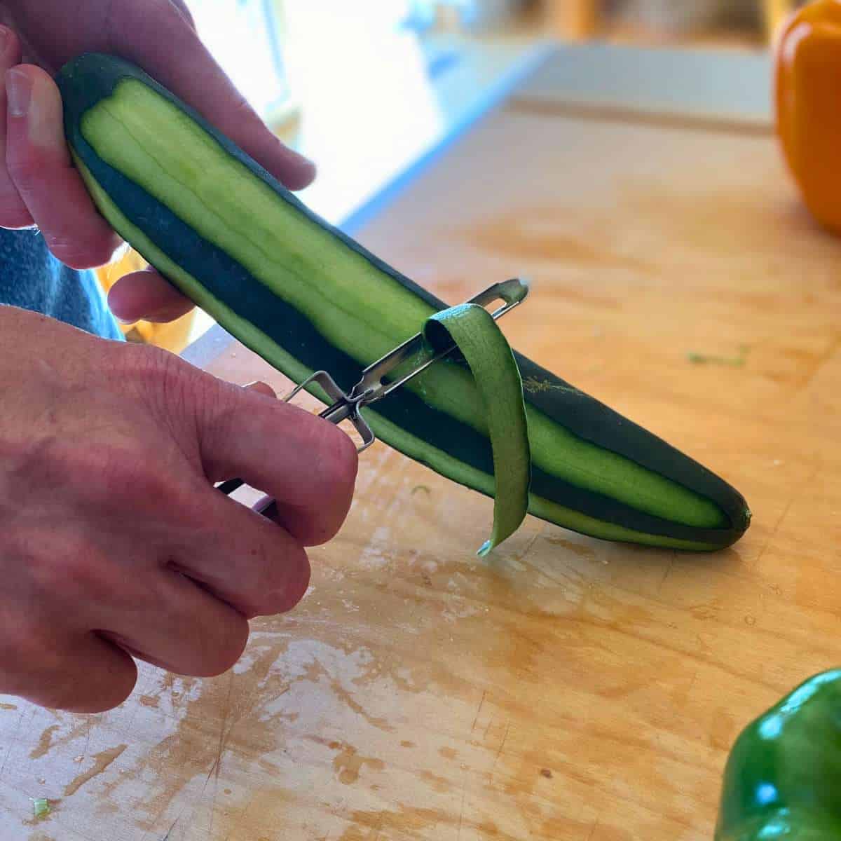 A vegetable peeler being used to remove strips of the skin of a cucumber.