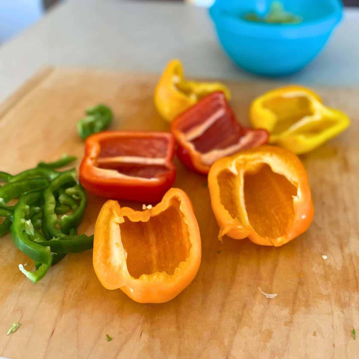 Orange, red, and yellow bell peppers cut in half lengthwise and green peppers in slices.