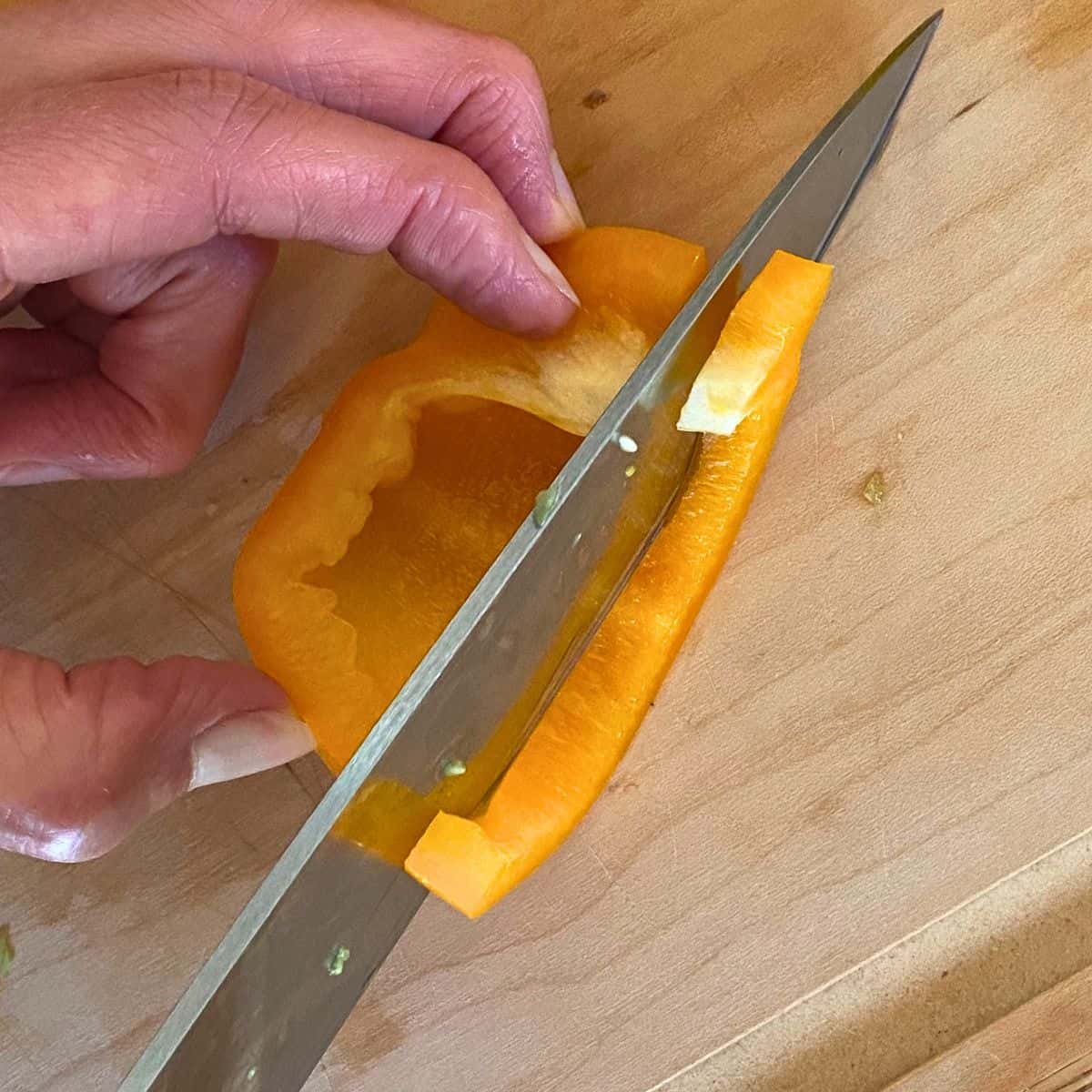 An orange pepper being sliced.