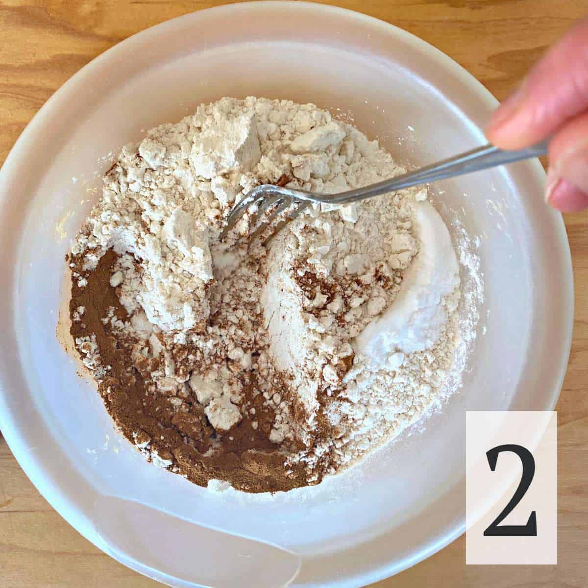 Gluten free flour, cinnamon, baking powder, baking soda, and salt being mixed with a fork in a bowl.