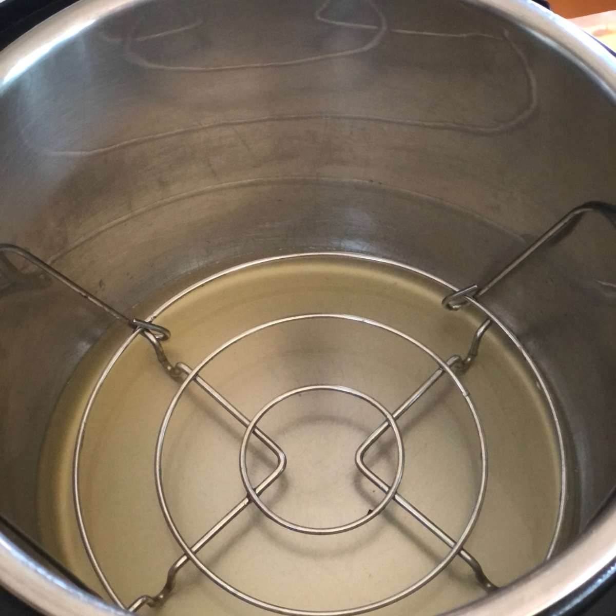 A pressure cooker pot with chicken broth and the trivet inside.
