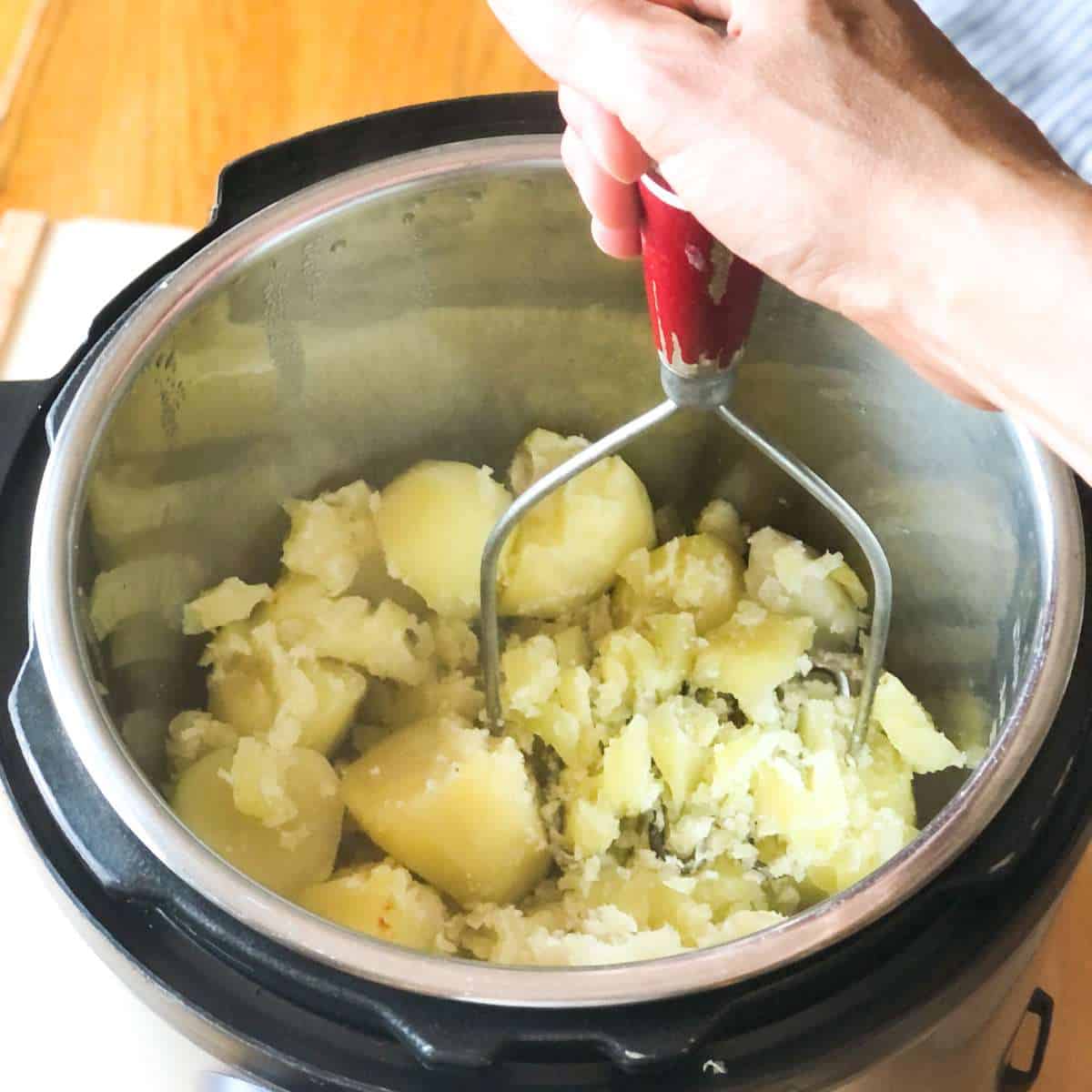 Cooked potatoes being mashed in a pressure cooker pot.