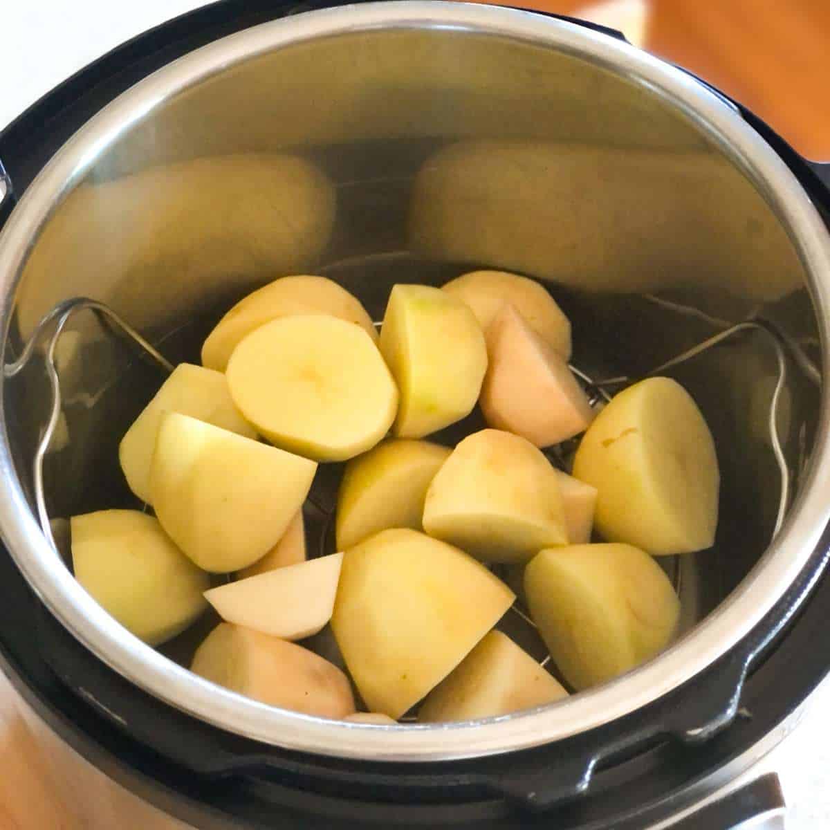 A pressure cooker pot with cut and peeled potatoes on a trivet inside.