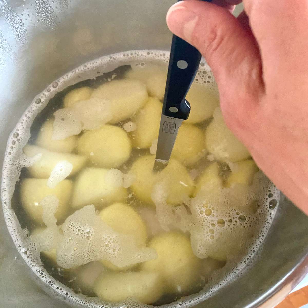 Potatoes in water being tested for doneness with a knife.