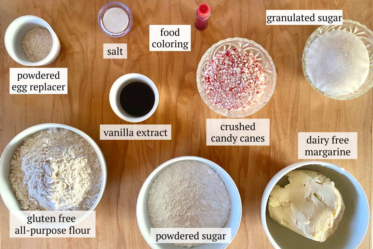 Ingredients needed to make gluten free candy cane cookies including gluten free flour, powdered sugar, dairy free margarine, vanilla extract, crushed candy canes, granulated sugar, powdered egg replacer, salt, and red food coloring
