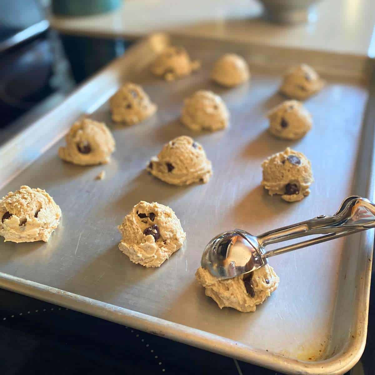 A cookie scoop placing cookie dough on a baking sheet.