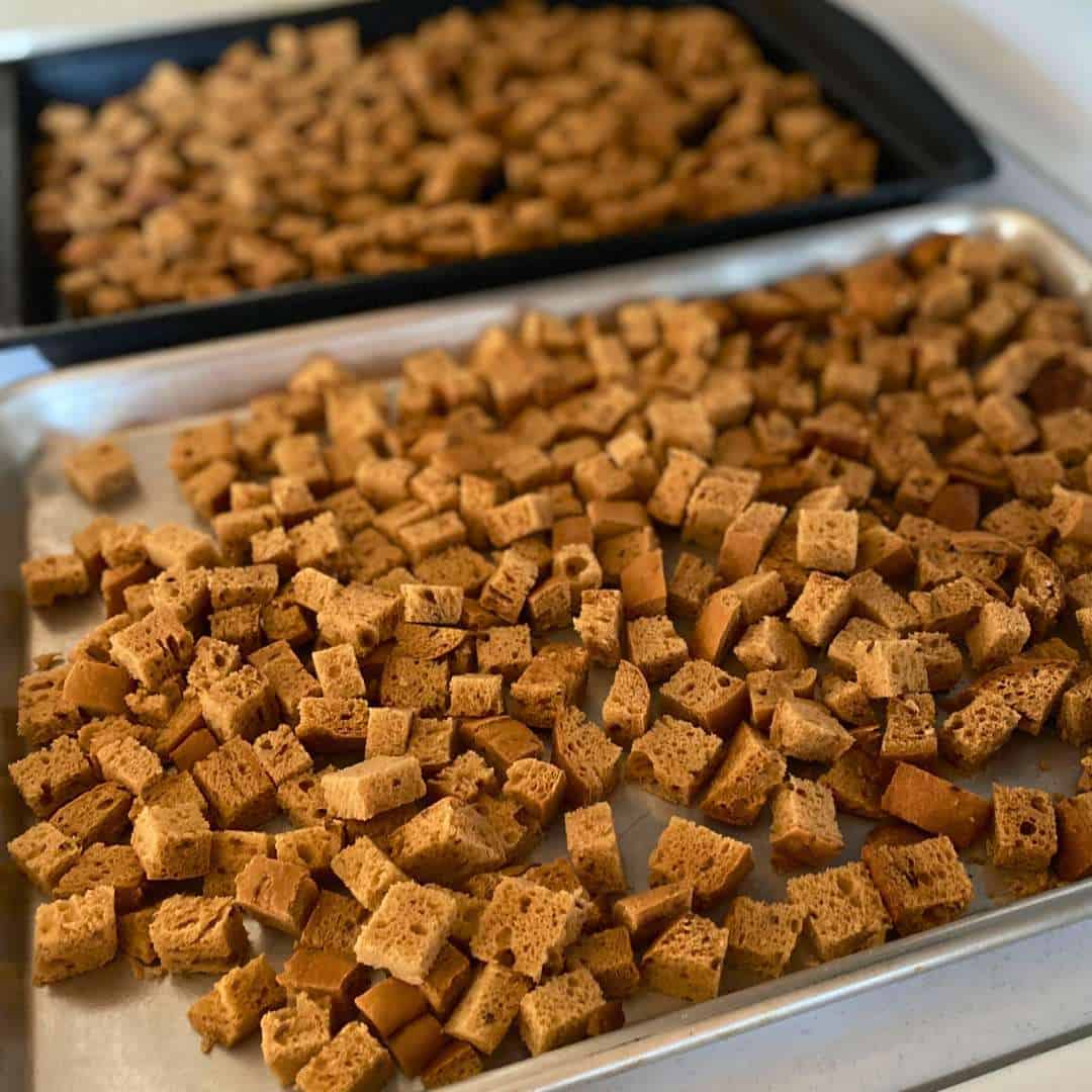 Gluten free bread cubes spread out on a baking sheet.